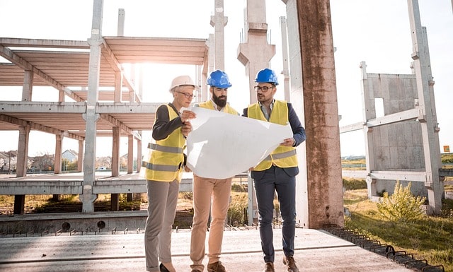 Image of 3 persons wearing safety gear and looking up design drawing on factory site